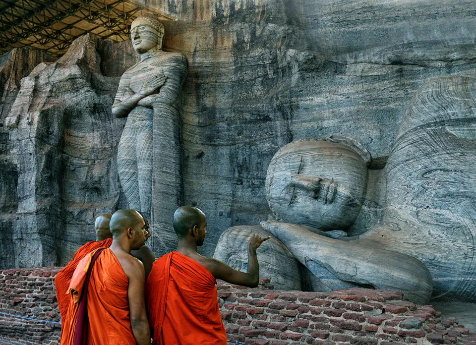Three monks in saffron robes before the standing and reclining Buddhas of Gal Vihara